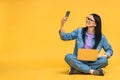 Business concept. Portrait of happy young woman in casual sitting on floor in lotus pose and holding laptop isolated over yellow Royalty Free Stock Photo