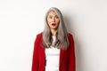 Business concept. Shocked senior female employer staring at camera speechless, standing in red blazer and makeup over