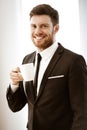 Business concept. Successful young businessman at work. Manager standing in office happy drinking coffee from cup. Man Royalty Free Stock Photo