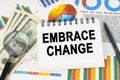 On the table are business charts, dollars and a notepad with the inscription - EMBRACE CHANGE