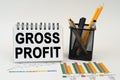 On the table are business charts, office supplies and a notepad with the inscription - gross profit