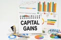 On the table are reports with graphs and a notepad with the inscription - Capital gains