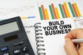 There is a calculator on the table, business charts, a man made a note in a notebook - Build Your Own Business