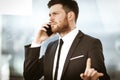 Business concept. Young businessman at the office standing and busy talking on a phone showing with hand he is resolving Royalty Free Stock Photo