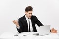 Business Concept: Young businessman working in bright office, sitting at desk, using laptop with serious facial Royalty Free Stock Photo