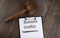 BUSINESS CONFLICT text on the paper with gavel on wooden background