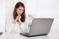 Business: confused woman in white sitting at desk looking at lap