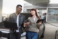 Business couple, Caucasian woman and African man, looking each other with smile, standing together outdoors near the car Royalty Free Stock Photo