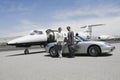 Business Couple Standing In Front Of Convertible And Private Jet