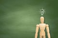 Wooden figure mannequin have light bulb on the head with green chalkboard on the background. Royalty Free Stock Photo