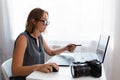 Business and creativity. Young woman in glasses working on a laptop. On the table is a camera and a tablet Royalty Free Stock Photo