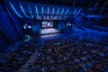 Business crowd attending international seminar in large blue illuminated auditorium