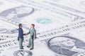 Business deal or agreement and success concept. Two miniature businessmen shaking hands while standing on american dollar money ba Royalty Free Stock Photo