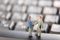 Business deal or agreement and success concept. Two miniature businessmen shaking hands while standing on the keys of a black keyb Royalty Free Stock Photo