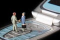 Business deal or agreement and success concept. Two miniature businessmen shaking hands while standing on the keys of a mobile pho Royalty Free Stock Photo