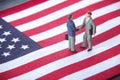 Business deal or agreement and success concept. Two miniature businessmen shaking hands while standing on USA american flag backgr Royalty Free Stock Photo
