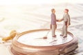 Business deal or agreement and success concept. Two miniature businessmen shaking hands while standing on vintage old clock and am Royalty Free Stock Photo