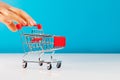 Business and e-commerce concept. Close-up of hand using fingers pushing an empty mini shopping trolley while standing over a blue