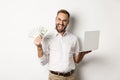 Business and e-commerce. Excited businessman holding money dollars and laptop, working online, standing over white Royalty Free Stock Photo