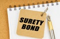 There are two notebooks and a pen on the table. On the top notepad, the inscription - SURETY BOND