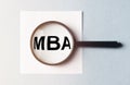 Business educatuion concept. paper sticker with text MBA acronym through magnifying glass on blue table, flatlay, master of