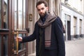 Business elegant man opens the door to his office. Stylish man in a coat with a beard enters the building with a bag in his hands. Royalty Free Stock Photo