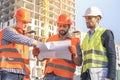 Business Engineers looking at blueprints. Male workers engineers at construction site in helmets hardhats near high-rise building Royalty Free Stock Photo