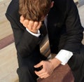 Desperate businessman sits sadly on a bank his hands folded over his head