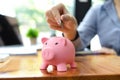 Business female employee putting coin in pink piggy bank