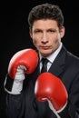 Business fighter. Portrait of confident businessman in red boxing gloves standing against black background Royalty Free Stock Photo