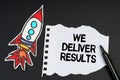 On a black background, a rocket, a marker and paper with the inscription - WE DELIVER RESULTS