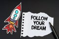 On a black background, a rocket, a marker and paper with the inscription - FOLLOW YOUR DREAM Royalty Free Stock Photo