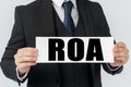 A businessman holds a sign in his hands which says ROA - RETURN ON ASSET Royalty Free Stock Photo