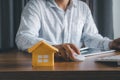 Business Finance concept. Close up yellow paper house model with young Asian man wear white shirt ongoing to working home loan