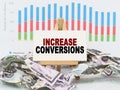 Among financial charts and money is a sign with the text - INCREASE CONVERSIONS