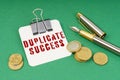 On a green surface, a pen, coins and a notepad with the inscription - Duplicate Success