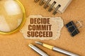 On the table are office items and a cardboard with the inscription - DECIDE COMMIT SUCCEED