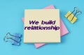On the table are paper clips, note paper with text - We build relationship