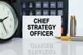 On the table there is a clock, a pen, a calculator and a business card on which the text is written - CHIEF STRATEGY OFFICER