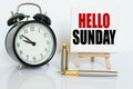 On the table there is a clock, a pen and a stand with a card on which the text is written - HELLO SUNDAY