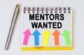 On a white background lie a pen and a notebook with the inscription - MENTORS WANTED