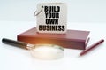 On the table there is a notebook, a pen, a magnifying glass and a notebook with the inscription Build your own business