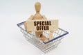 A wooden man sits in a shopping basket, holding a sign in his hands - SPECIAL OFFER