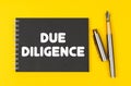 On a yellow background lies a pen and a black notebook with the inscription - Due Diligence Royalty Free Stock Photo