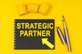 On a yellow background lies a pen, a black notebook with the inscription - STRATEGIC PARTNER