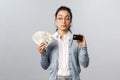 Business, finance and investment concept. Thoughtful indecisive cute asian girl look tempting at cash dollars, holding Royalty Free Stock Photo