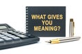 On a white background, there is a calculator, a pen and a black notebook with the inscription - WHAT GIVES YOU MEANING