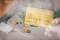 Business and financial concept. Double exposure hand holding credit card and wooden home with small people model stand on a stack Royalty Free Stock Photo
