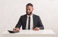 Black entrepreneur sitting at workdesk and using calculator