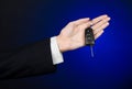 Business and gift theme: car salesman in a black suit holds the keys to a new car on a dark blue background in studio Royalty Free Stock Photo